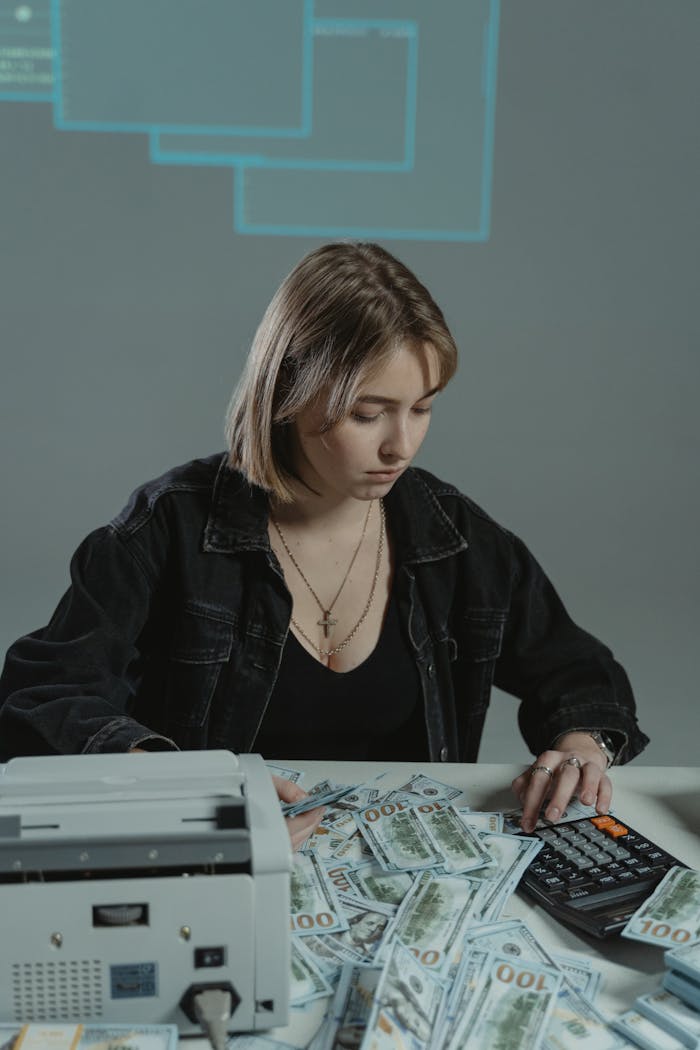 Focused woman calculating money with stacks of banknotes and a calculator indoors.