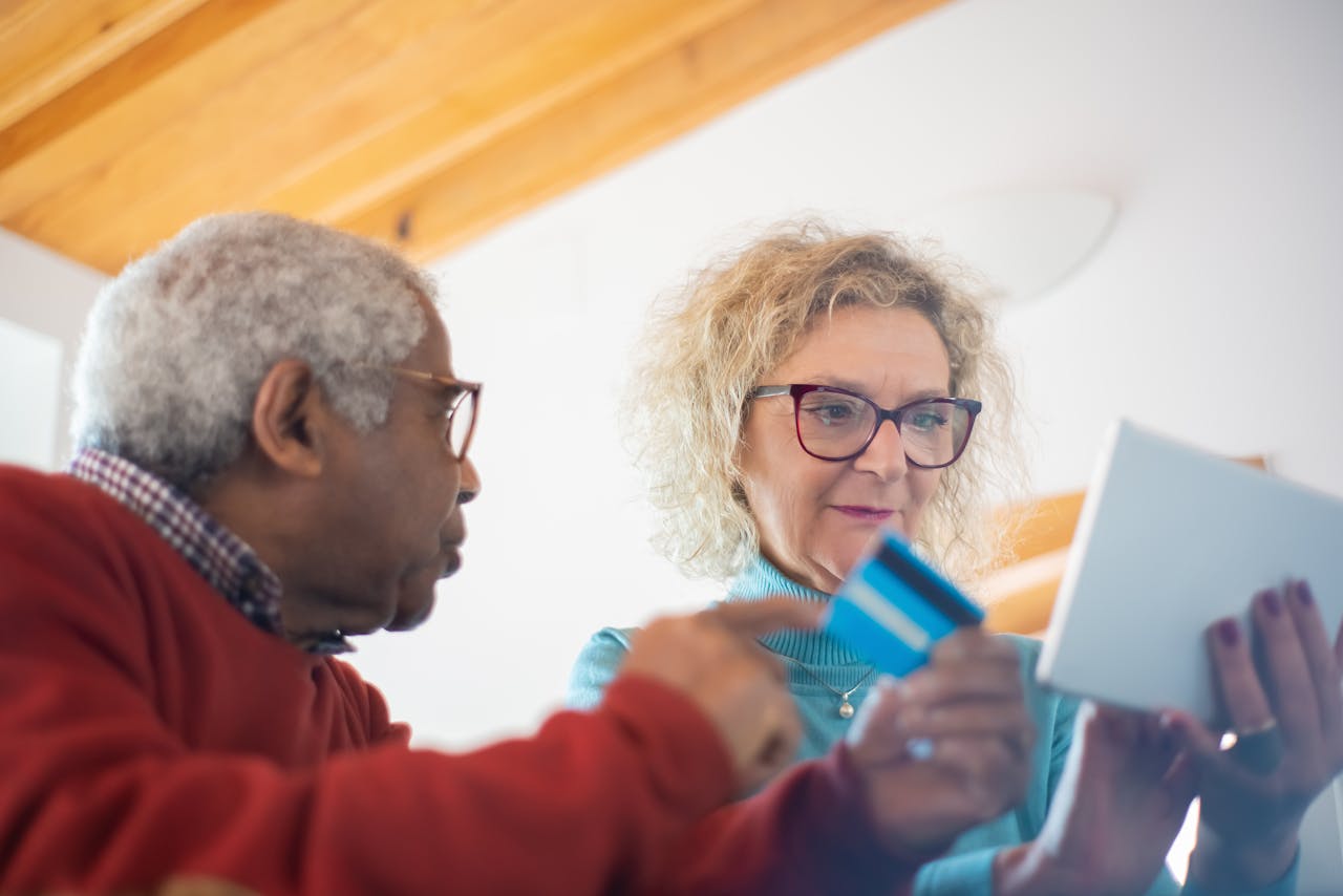 Senior adults using a tablet and credit card for online shopping indoors.